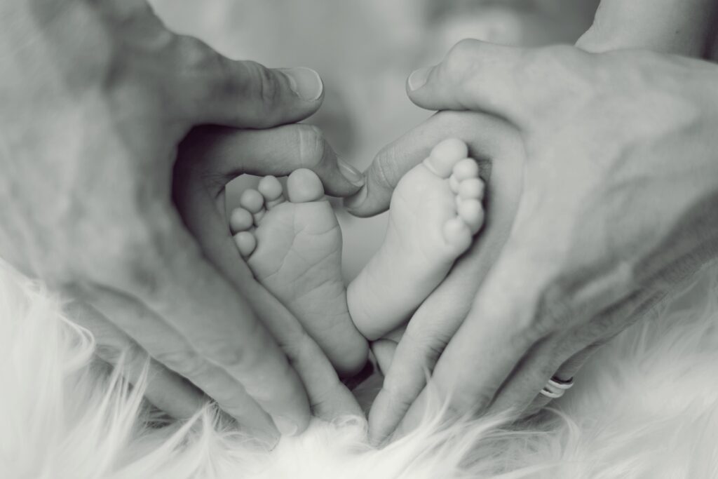 Ruce matky a otce obepínají dětské nožičky do tvaru srdce.