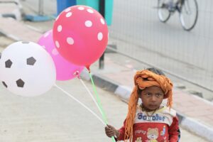 Dítě držící červený bílý a růžový balónek.