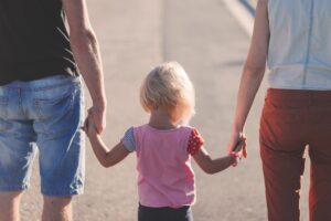 Otec na levé straně drží malou blond holčičku za ruku a z pravé strany ji drží za ruku maminka.