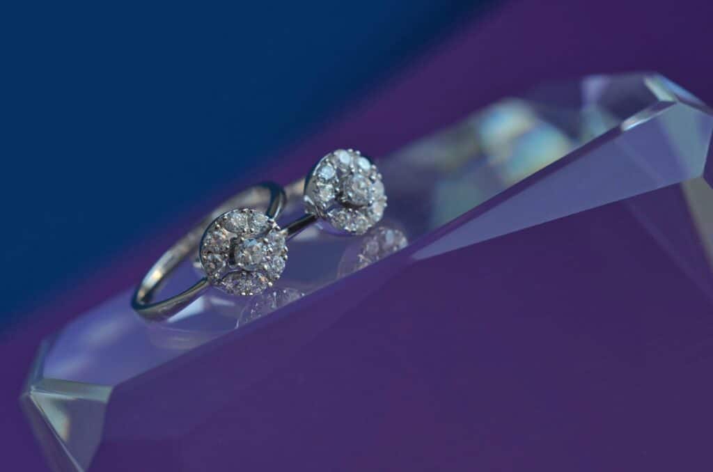 Zásnubní prstýnek s diamantem položený na skleněném tácku s fialovým pozadím