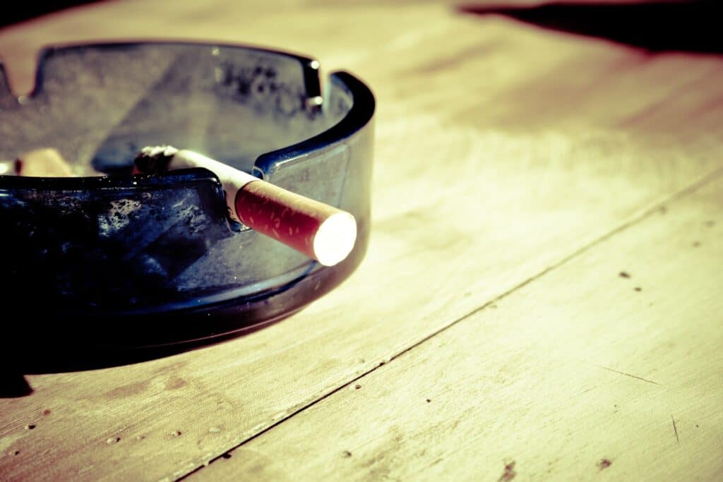 Rozkouřená cigareta ve skleněném popelníku na dřevěném stole.