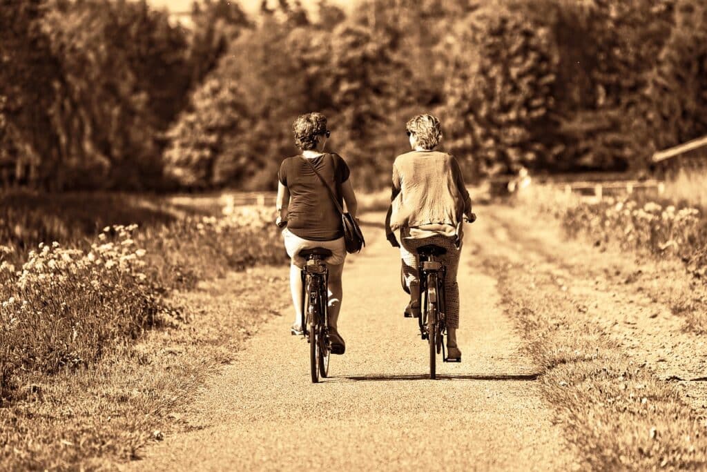 Sépiový obrázek, na kterém jsou dvě přítelkyně jedoucí na kole po polní cestě.
