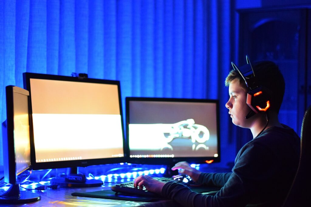 Chlapec hraje počítačové hry na třech monitorech.