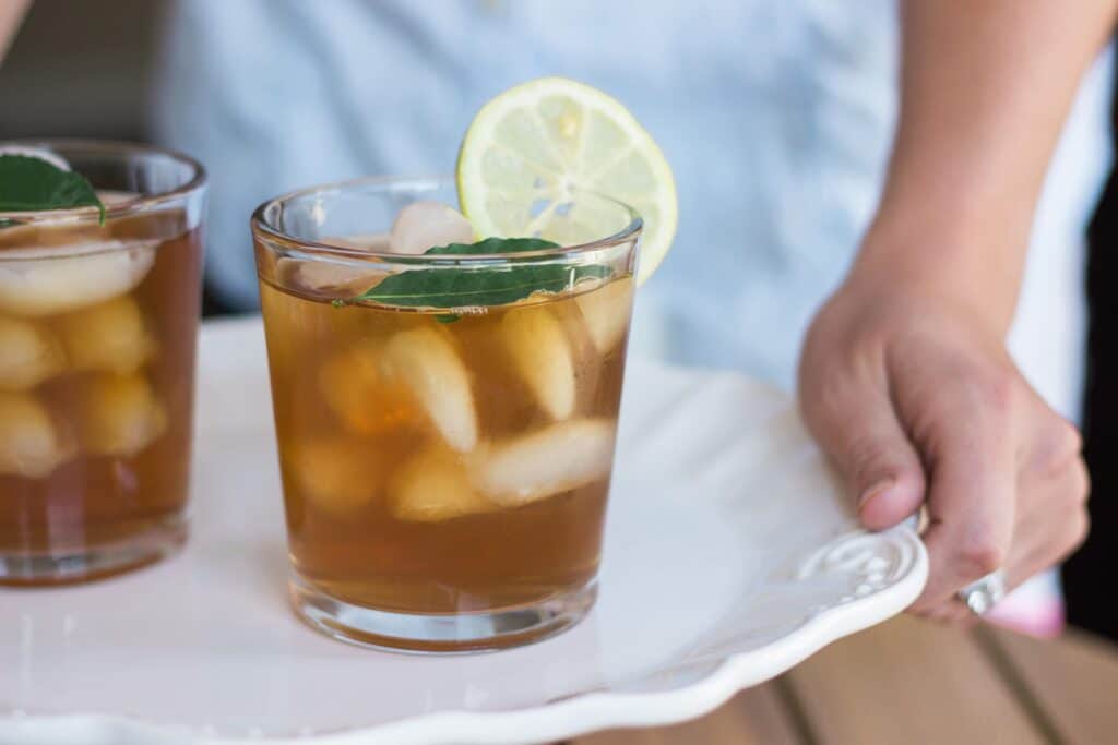 2 sklenice s ledovým čajem, mátou a citrónem na skleněném podnose, který nese obsluha.
