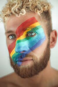 Obličej muže, jehož tvář je nabarvena duhovými barvami v symbolu gay komunity.
