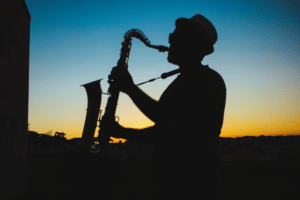 Silueta jazzového hráče na saxofon při západu slunce.