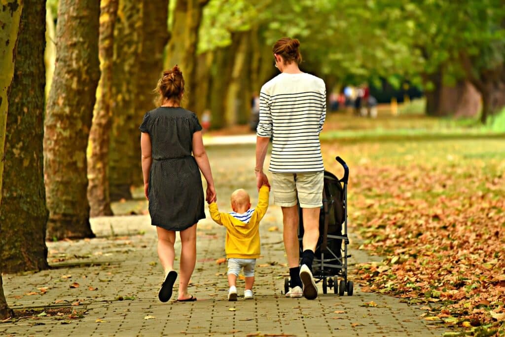 Matka a otec na procházce parkem s dítětem, které je drží za ruce a je uprostřed.