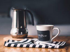 Kavový hrnek položený na utěrce a za ním je postavená konvice na kávu.