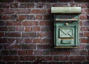 Ocelově zelená poštovní schránka na cihlové zdi.