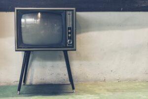 Stará krabicová televize položená na televizním stolku.