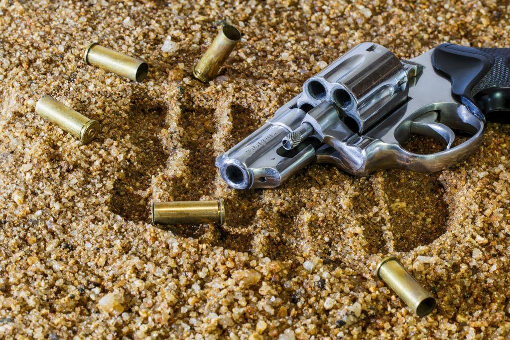 Zbraň pohozená v písku a okolo ní je 5 kulek.