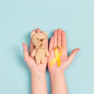 Dvě dlaně- jedna s medvídkem, druhá se stuhou v barvách symbolizujících dětskou rakovinu.