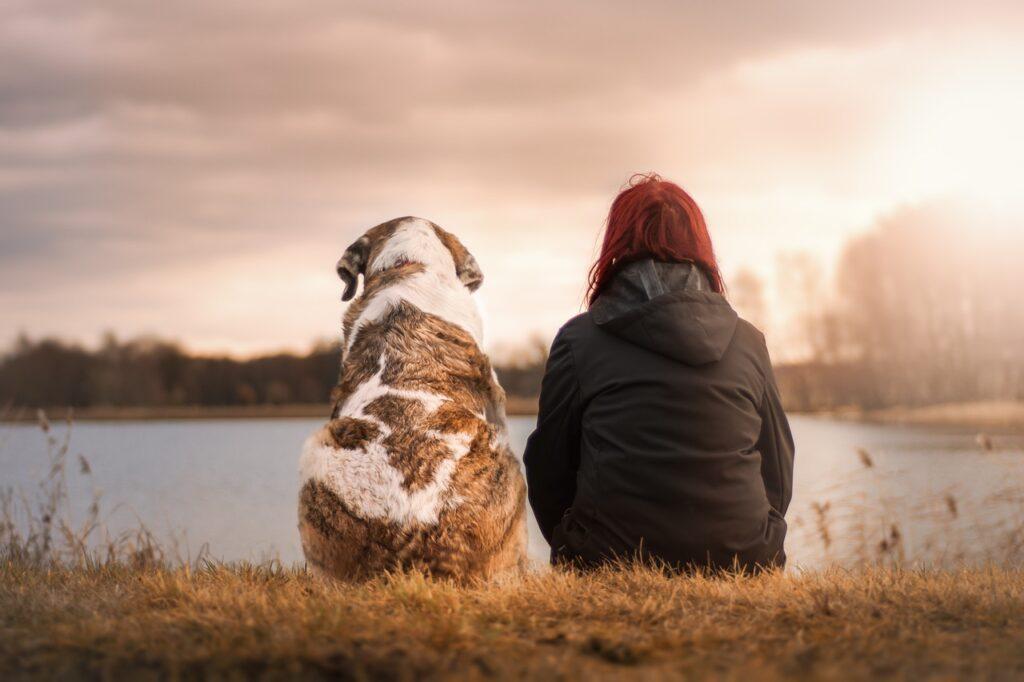 Žena a pes sedící na břehu jezera.